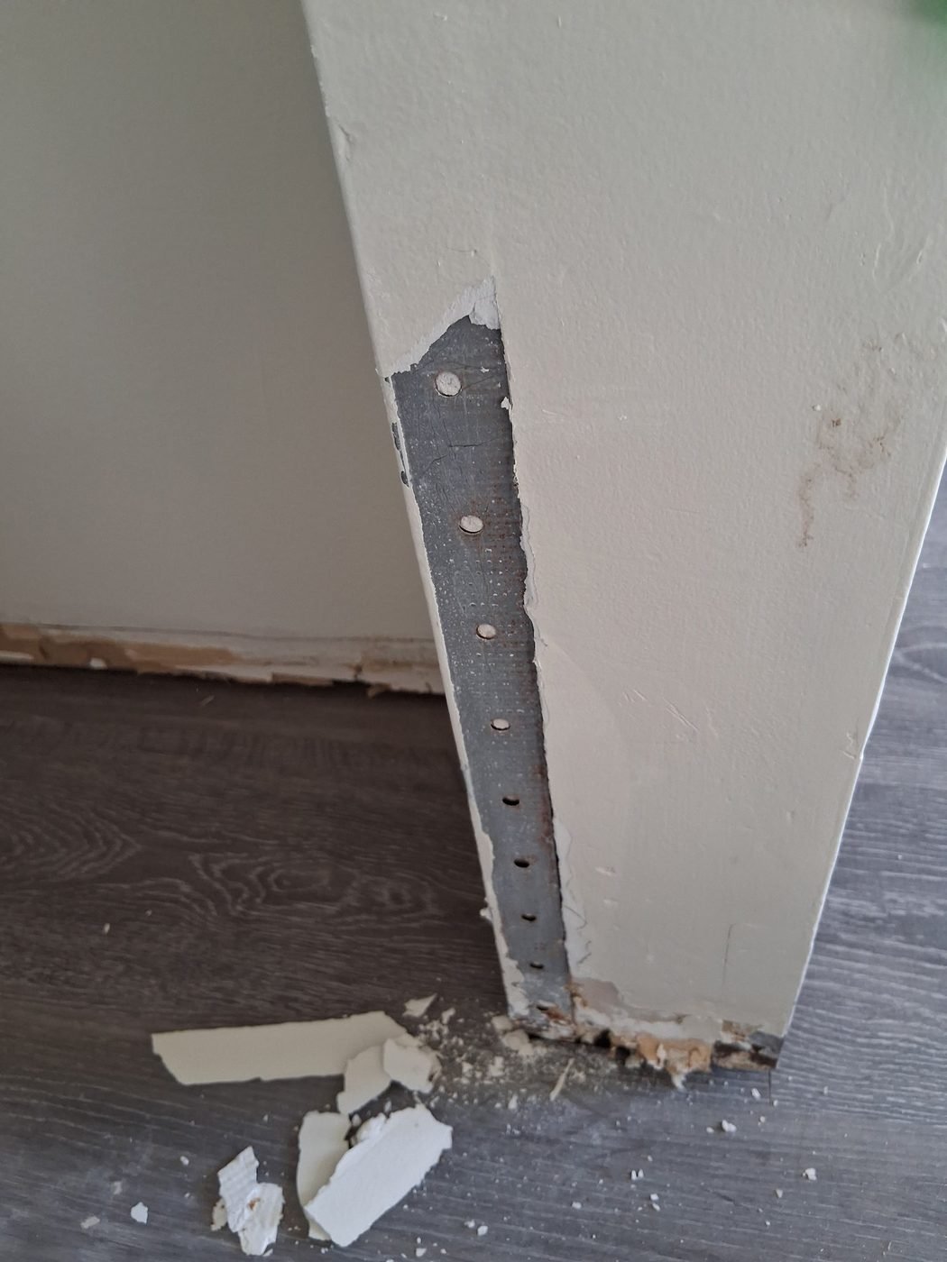 Damaged outside wall corner with the metal corner bead exposed and rusting