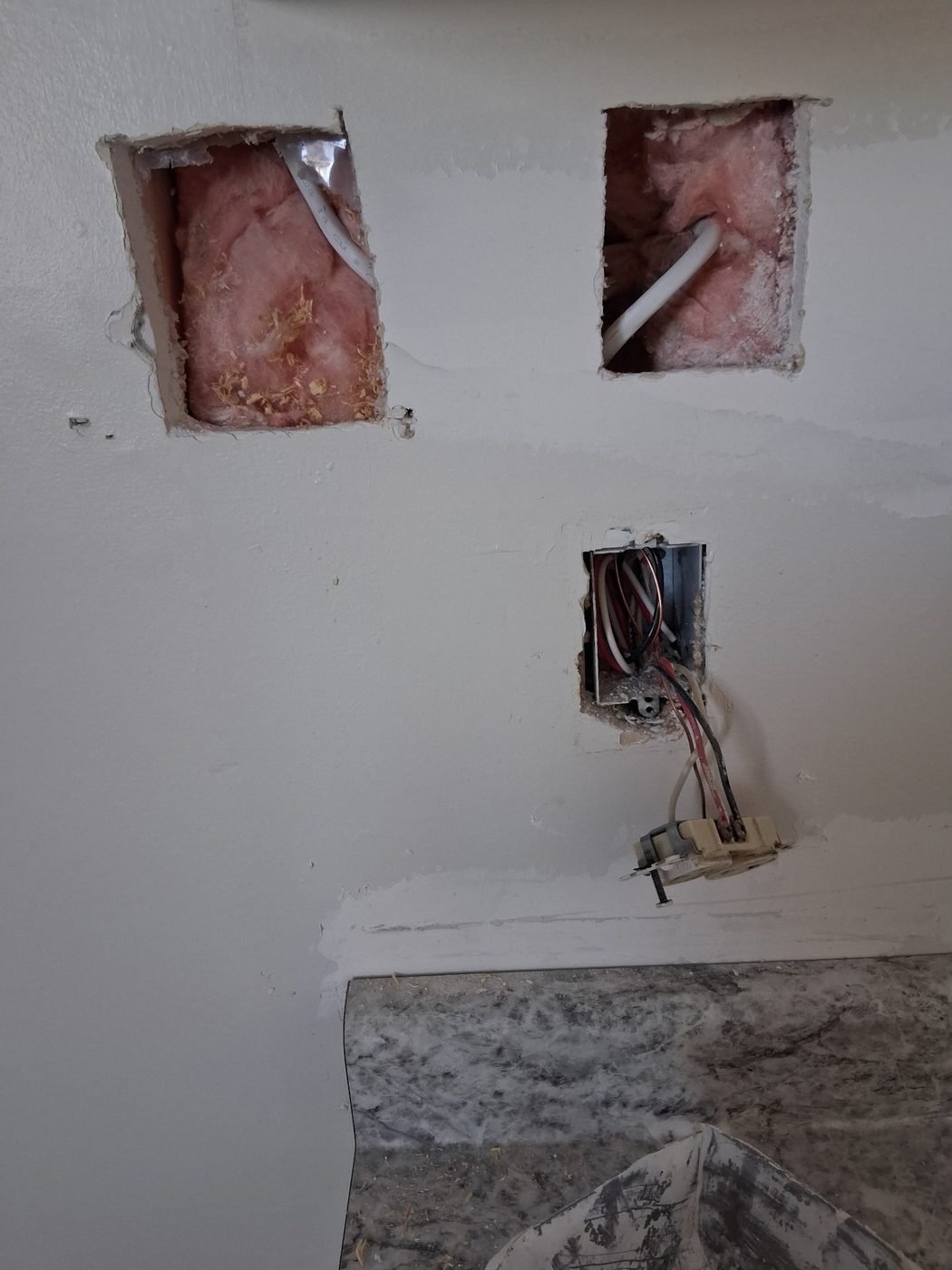 Two rectangular access cuts in a wall showing insulation and electrical wiring