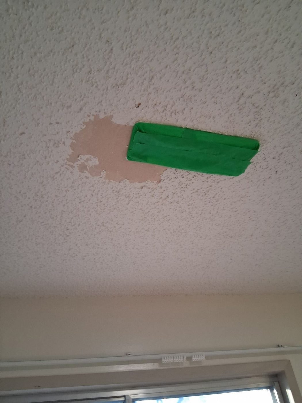 Textured ceiling scraped back around a repair and masked off